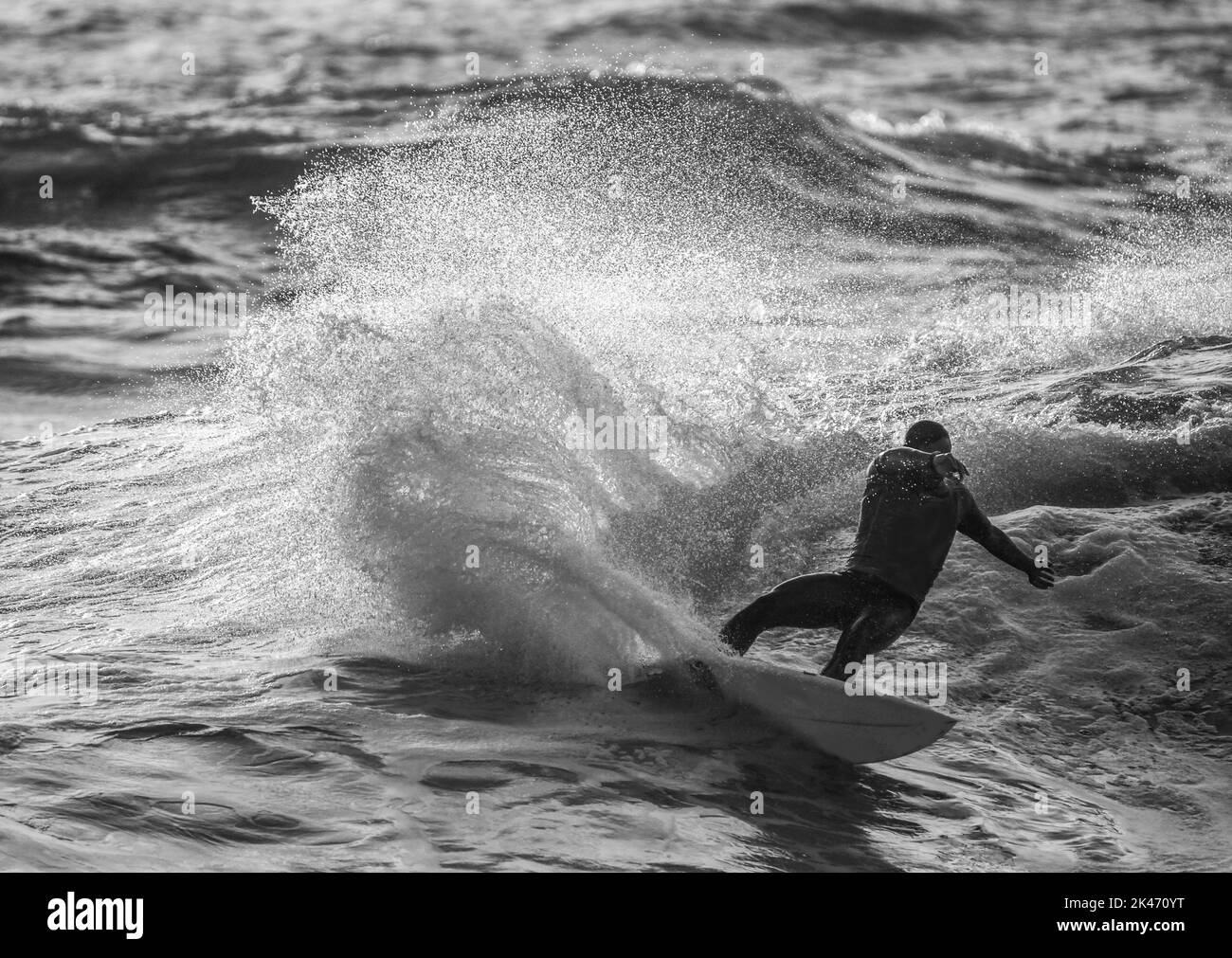 Surfer se déplace rapidement avec de grandes éclaboussures quantityof. Le surfeur cache son visage à la main si méconnaissable. Côte d'InGood du Portugal. Photo monochrome. Banque D'Images