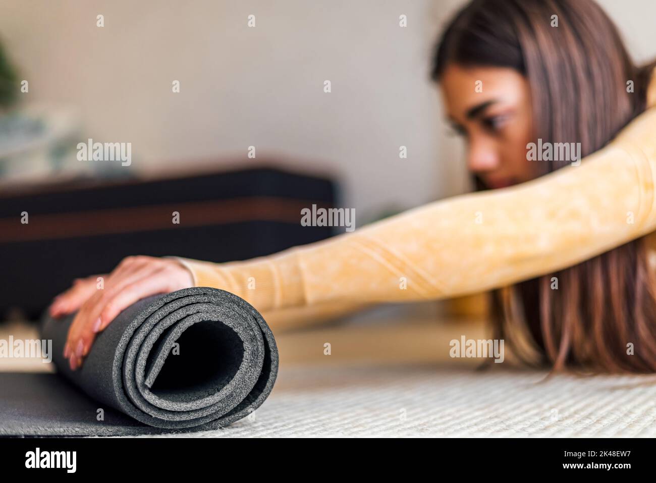 Photo d'une jeune femme brune adulte, mettant son tapis de yoga en mousse après l'entraînement. Banque D'Images