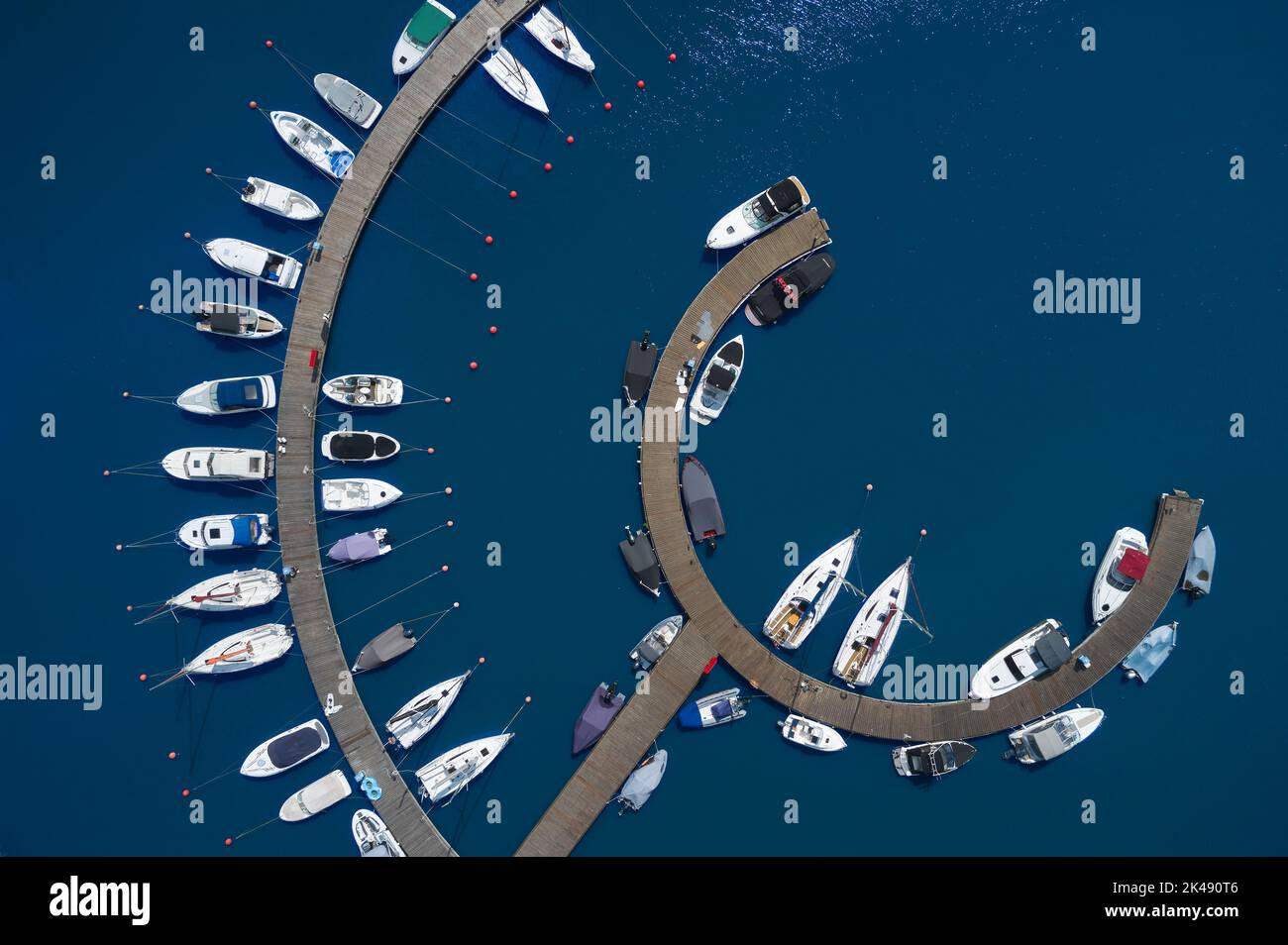 Vue aérienne des bateaux amarrés le long d'une jetée courbe sur l'eau bleue. Banque D'Images
