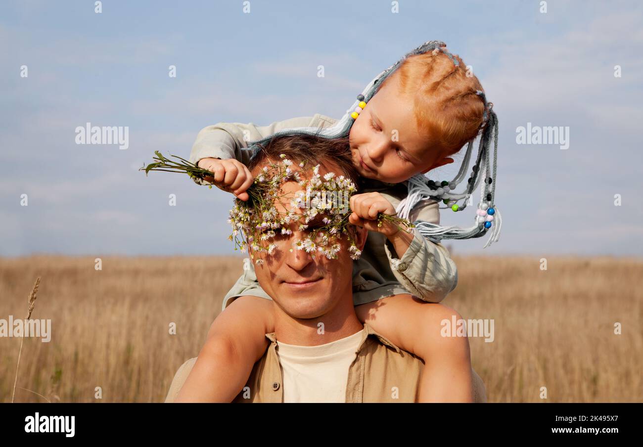 Papa et fille. L'homme joue avec une petite fille dans la nature. Enfant aux cheveux rouges près des yeux des pères avec des fleurs Banque D'Images