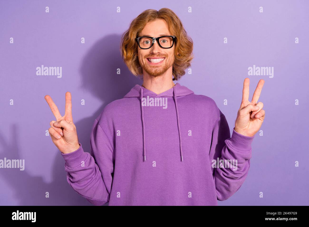 Photo d'optimiste curly rouge coiffure Guy show v-sign porter oculaire violet sweatshirt isolé sur fond violet couleur Banque D'Images