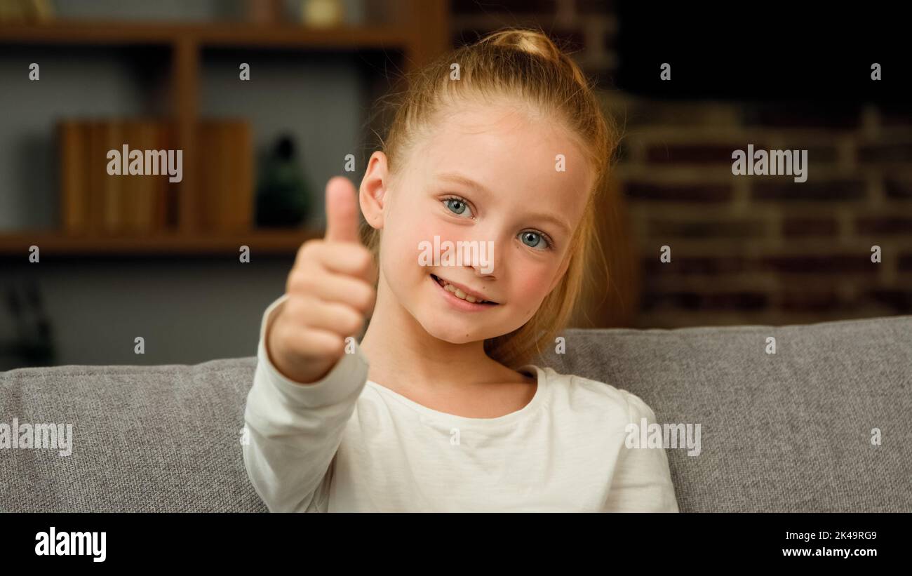 Portrait caucasien heureux satisfait blonde fille petit enfant positif enfant regardant l'appareil-photo faire le pouce vers le haut et l'approbation geste tout bien Banque D'Images
