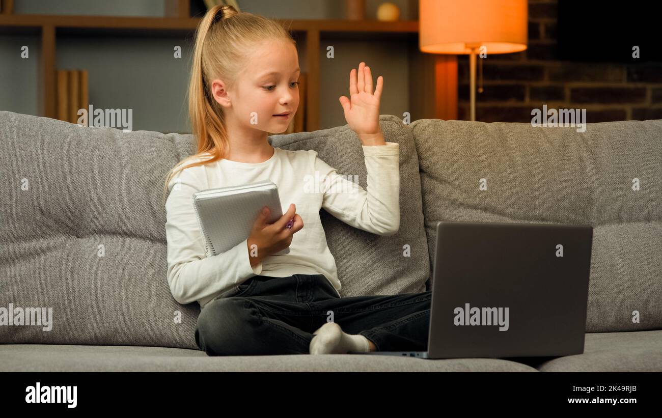 Blonde petite fille intelligente élève d'école écouter la leçon éducative sur ordinateur portable à la maison en ligne réunion de classe dans le chat vidéo pendant la pandémie écrire des devoirs Banque D'Images