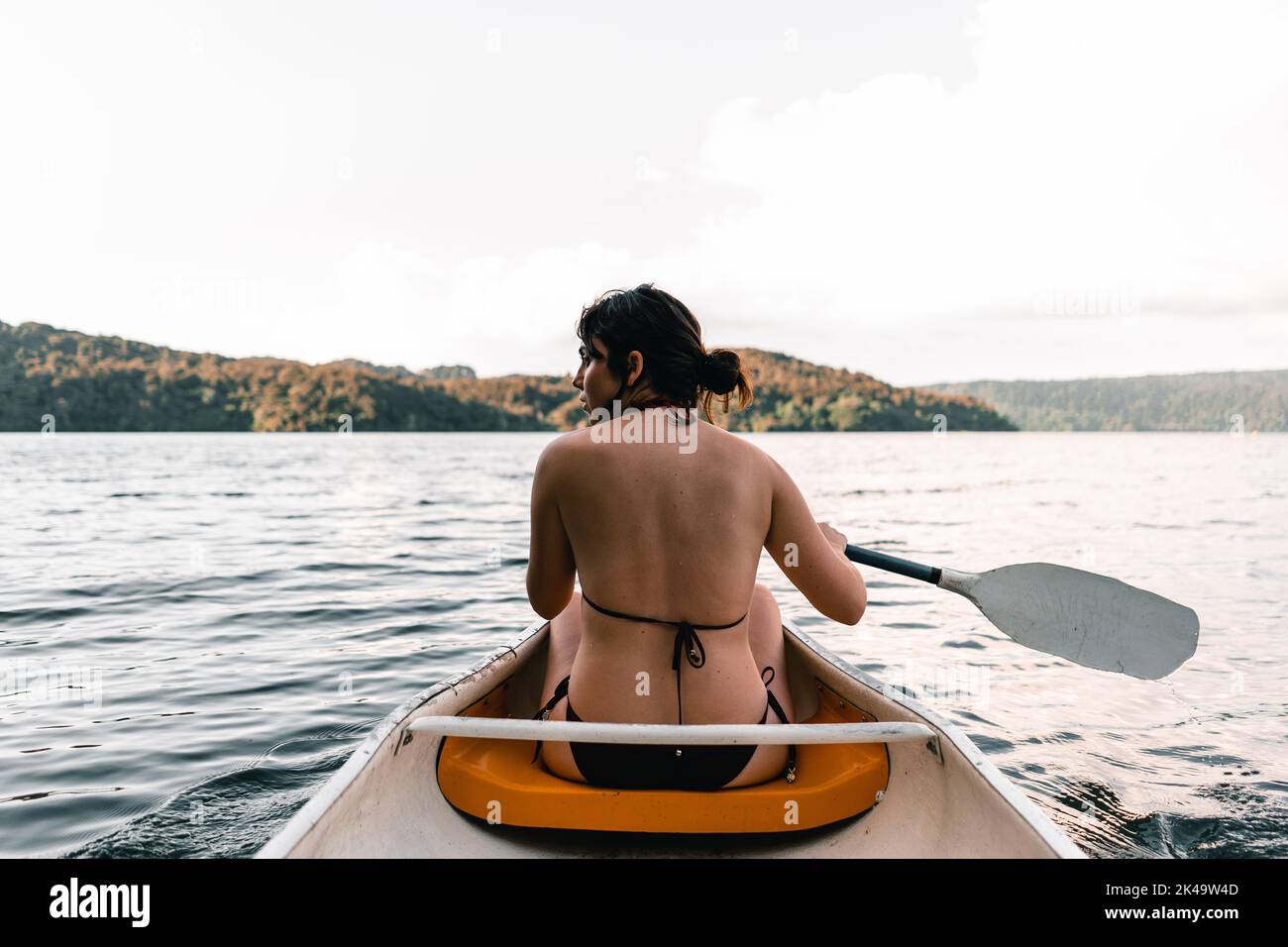 fille caucasienne portant un maillot de bain assis à l'intérieur d'un kayak sur son dos et regardant le côté pagayer sur le lac vers l'île, le lac tarawera Banque D'Images