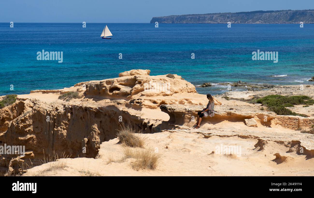 Vue panoramique d'une femme assise sur des rochers tout en regardant un voilier sur la mer. Île de Formentera, Espagne Banque D'Images