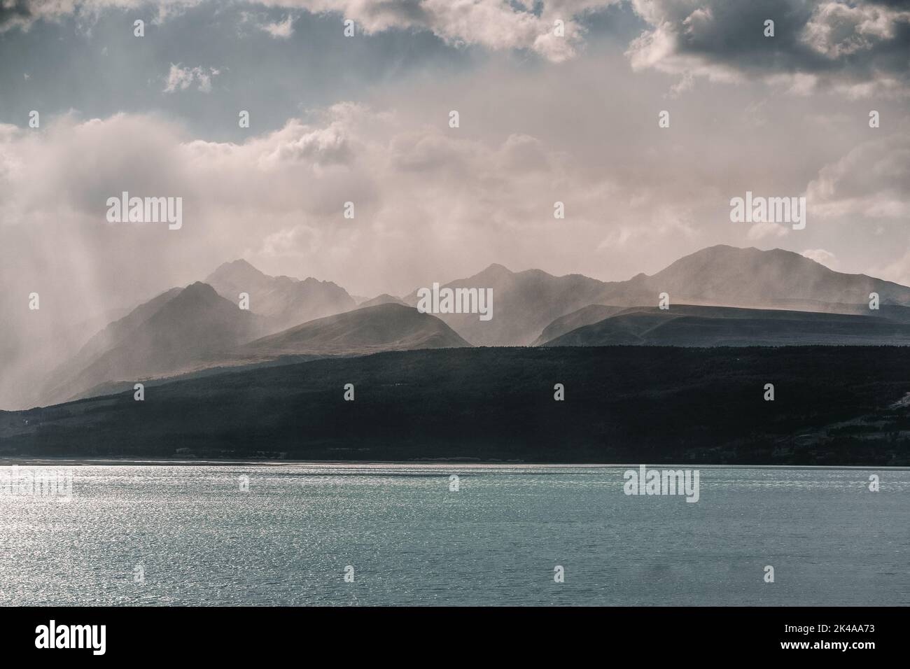 mer ​​water paysage avec de nombreuses montagnes en arrière-plan et le soleil se reflétant dans l'eau sous un ciel gris pluvieux et noir avec beaucoup Banque D'Images