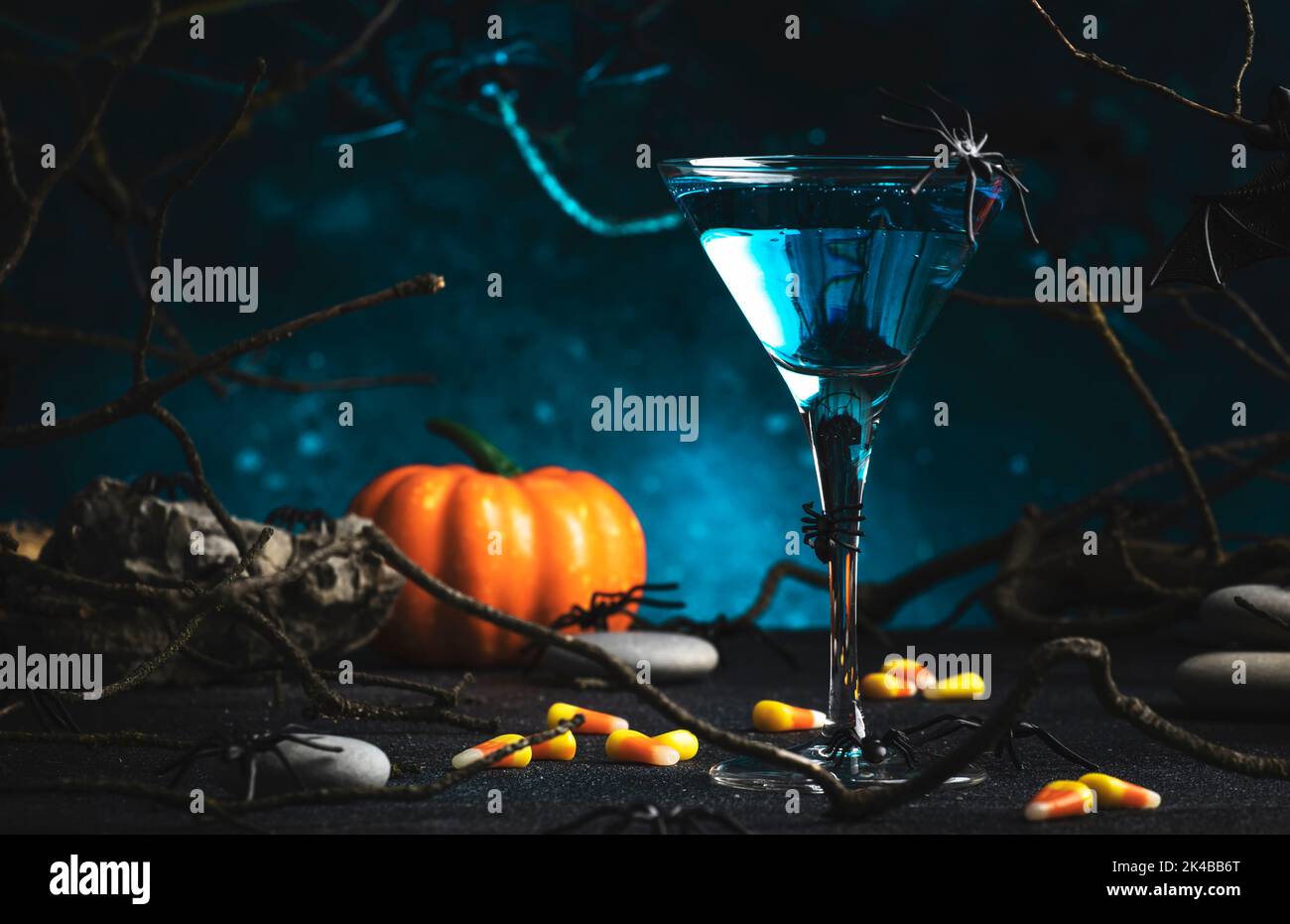 Cocktail alcoolique de martini d'Halloween sur fond bleu foncé effrayant avec branches tordues, chauves-souris, pierres et araignées, boisson de fête pour la fête Banque D'Images