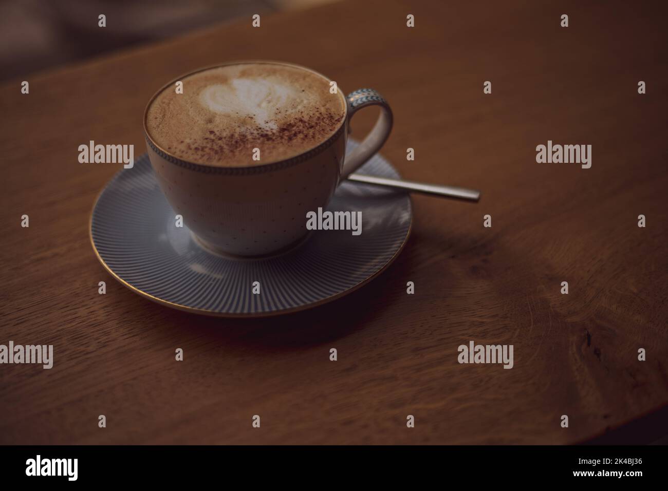 Tasse de café avec un motif de coeur dans une tasse sur une soucoupe sur un fond en bois dans un café. Banque D'Images