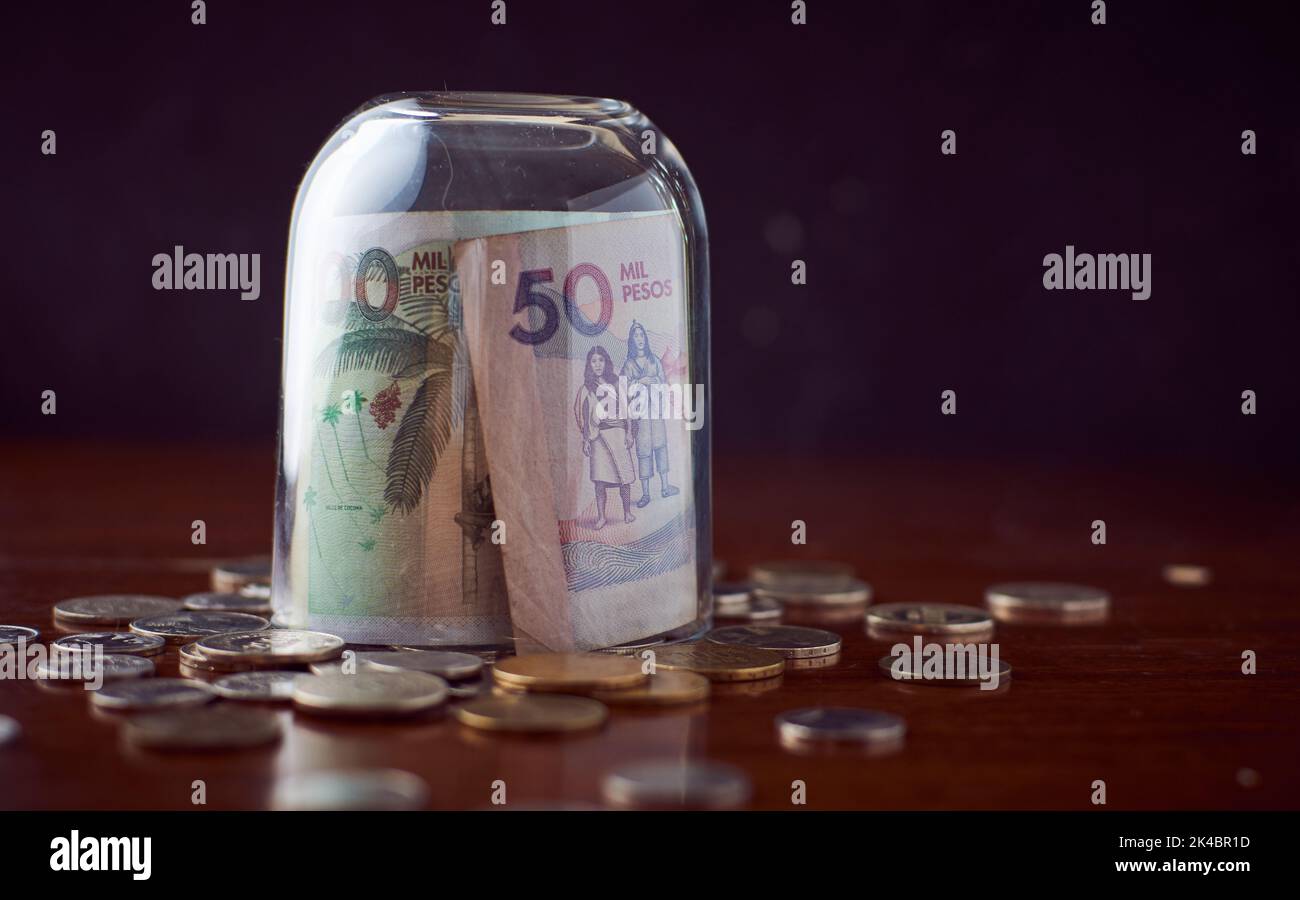 Une tasse de verre de fermeture sur des billets de Colombia Peso sur une table en bois avec des pièces de monnaie Banque D'Images