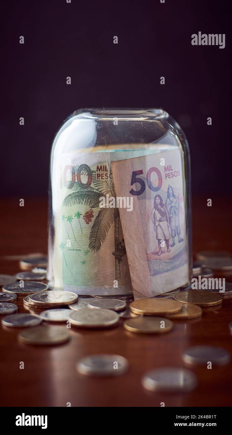 Une tasse de verre de fermeture sur le peso de Colombie espèces sur une table en bois avec des pièces de monnaie, avec fond sombre Banque D'Images