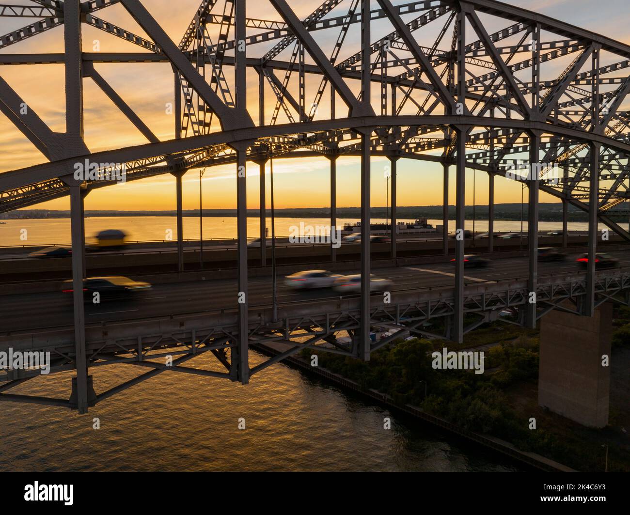 Un grand pont de treillis sur une vaste étendue d'eau est vu au coucher du soleil comme les voitures, mouvement flou, Voyage à travers l'autoroute à plusieurs voies. Banque D'Images