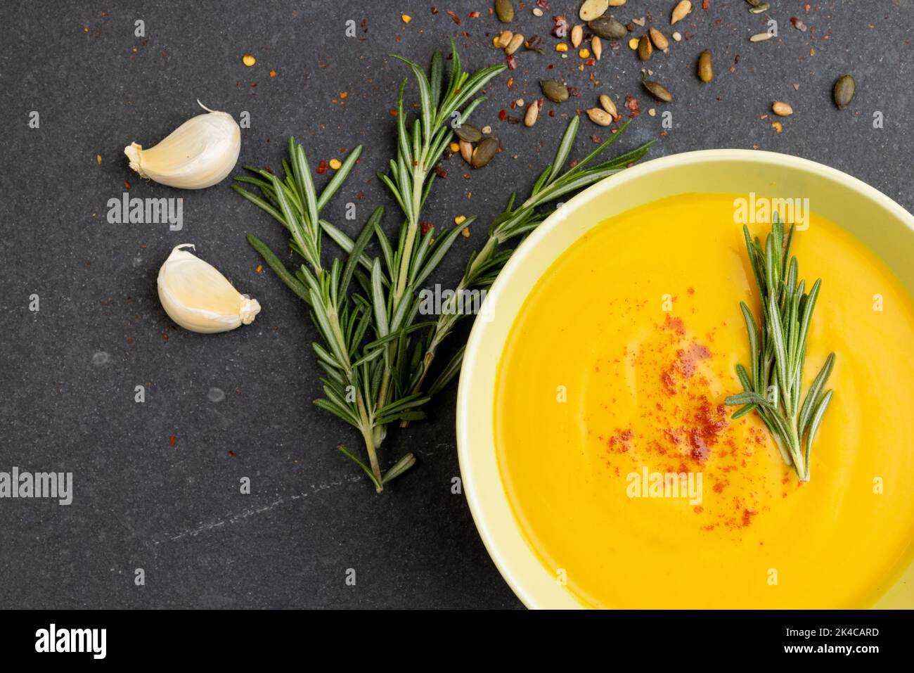 Image horizontale d'un bol de soupe aux carottes avec garniture au romarin, gants à l'ail et graines sur ardoise Banque D'Images