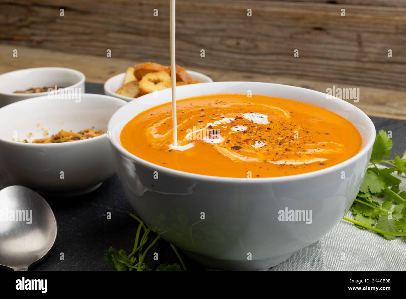 Image horizontale de la crème versé dans un bol de soupe aux tomates, avec pain grillé et feuilles Banque D'Images