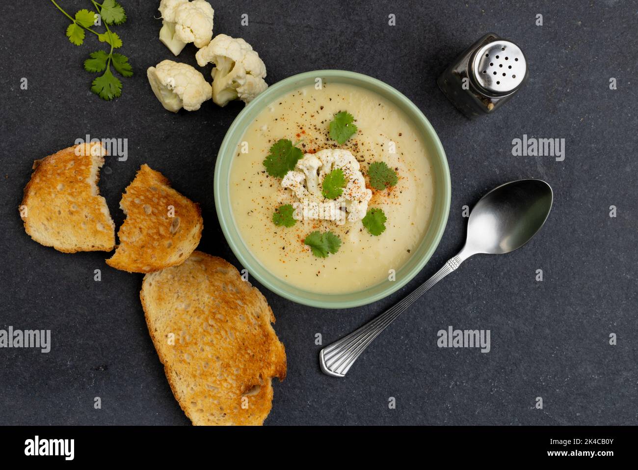 Image horizontale d'un bol de soupe de chou-fleur avec garniture, avec toasts et fleurs sur ardoise Banque D'Images Image horizontale d'un bol de soupe de chou-fleur avec garniture, avec toasts et fleurs sur ardoise Banque D'Images