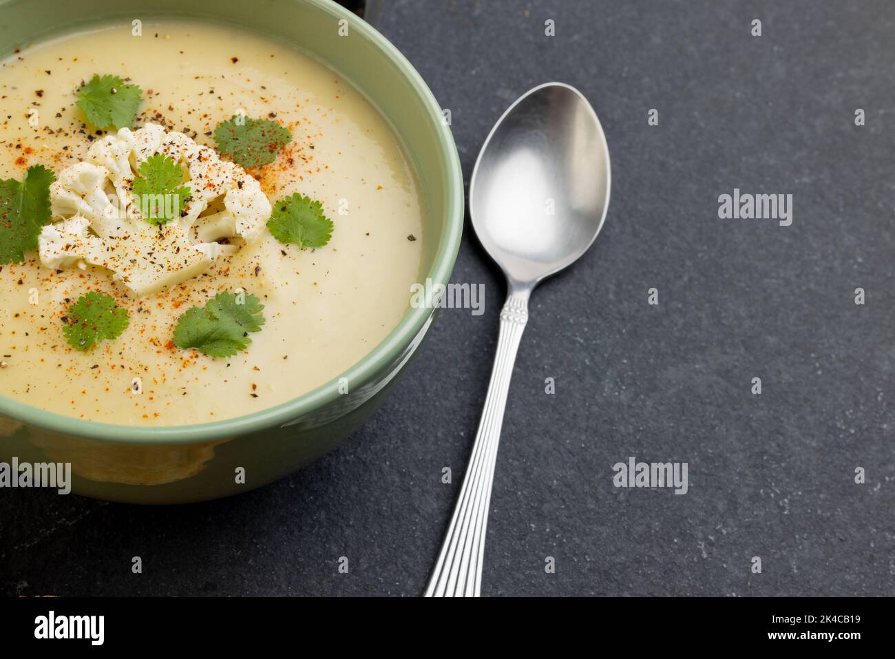Image horizontale d'un bol de soupe de chou-fleur avec garniture, avec cuillère sur ardoise, avec espace de copie Banque D'Images Image horizontale d'un bol de soupe de chou-fleur avec garniture, avec cuillère sur ardoise, avec espace de copie Banque D'Images