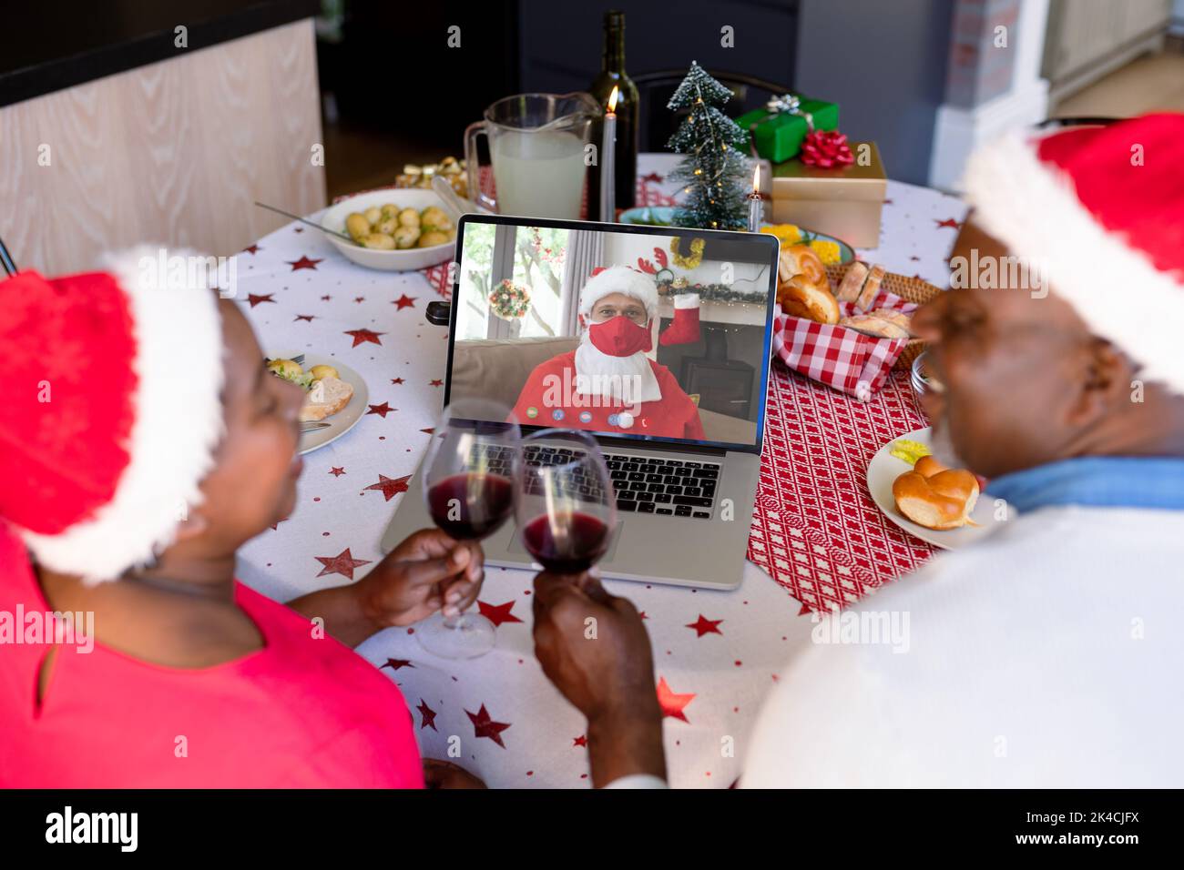 Couple senior afro-américain avec vigne lors de l'appel vidéo de noël avec le père noël en face maks. noël, festivité et technologie de communication duri Banque D'Images