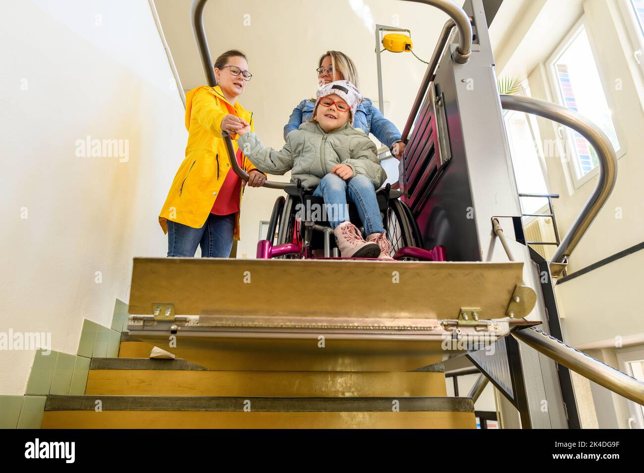 Mère avec un jeune enfant vivant avec une paralysie cérébrale utilisant un ascenseur électrique pour fauteuil roulant pour accéder au bâtiment public. Plate-forme de levage spéciale pour fauteuil roulant Banque D'Images