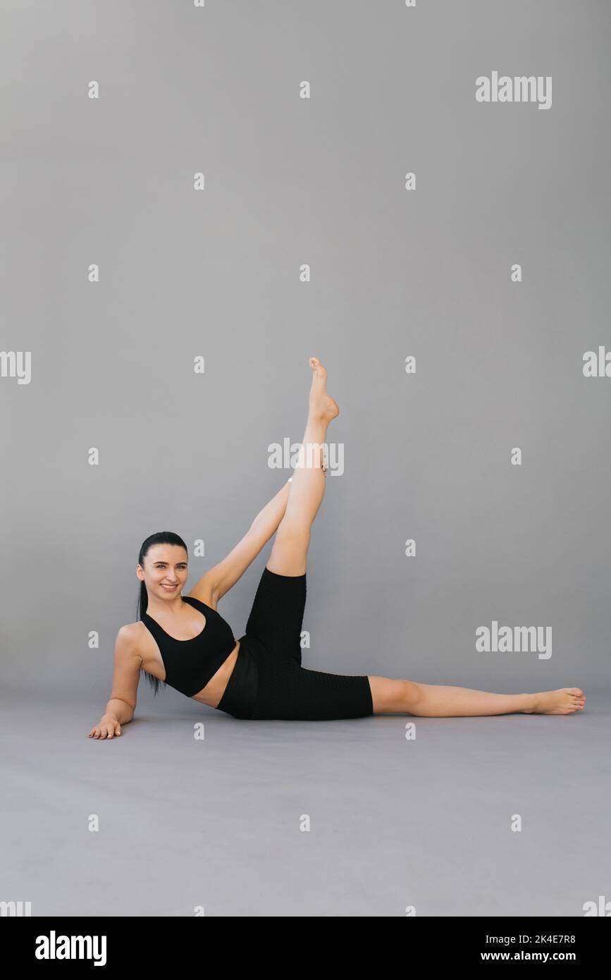 Femme fait du sport. Une brunette en noir sportswear fait un exercice de yoga ou de fitness, elle est allongée sur son côté avec sa jambe relevée, gr isolé Banque D'Images
