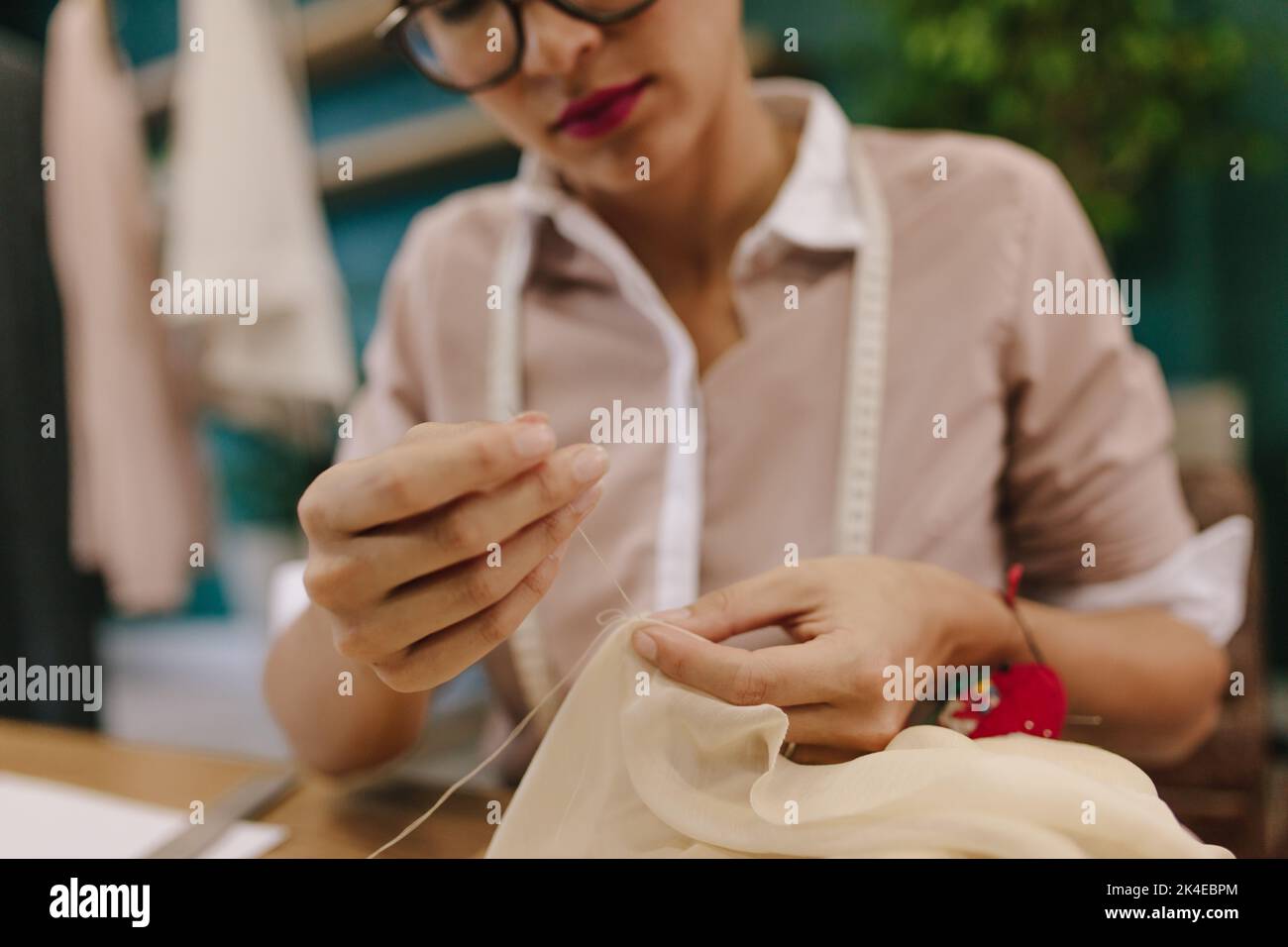 Gros plan de femme mains couture robe de designer à son lieu de travail. Femme de mode travaillant dans son studio. Les mains du couturier font du travail à main sur le dre Banque D'Images