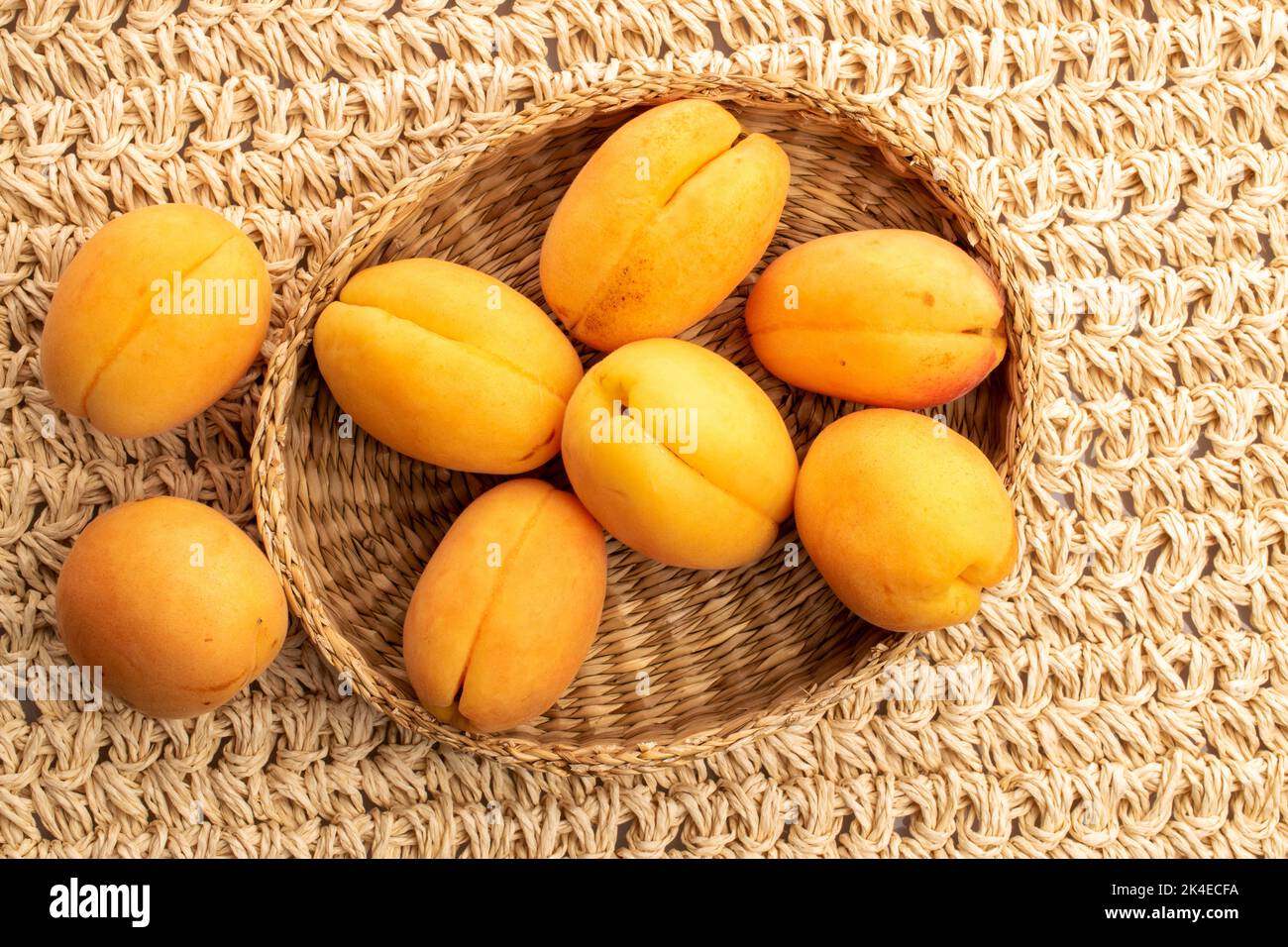 Plusieurs abricots jaunes d'ananas dans une assiette de paille, macro, sur un tapis de paille, vue de dessus. Banque D'Images