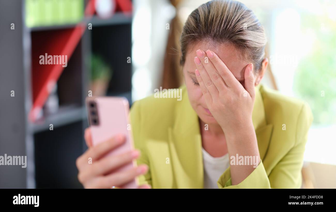 Triste fille bouleversée de lire de mauvaises nouvelles dans un message mobile sur smartphone dans le bureau à table Banque D'Images