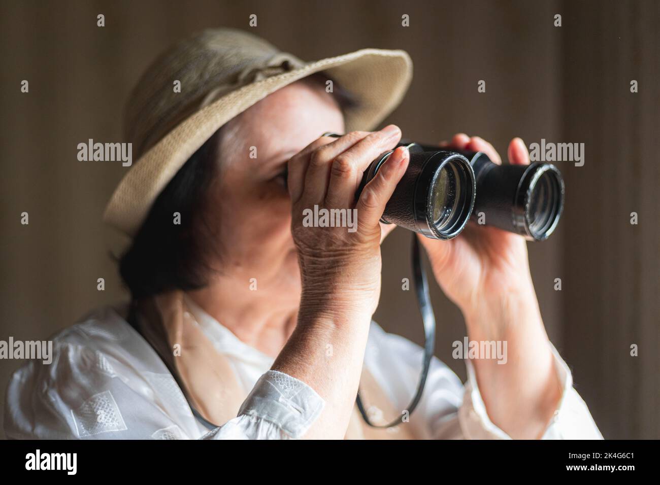 Femme âgée regardant à travers les jumelles, l'espionnage Banque D'Images