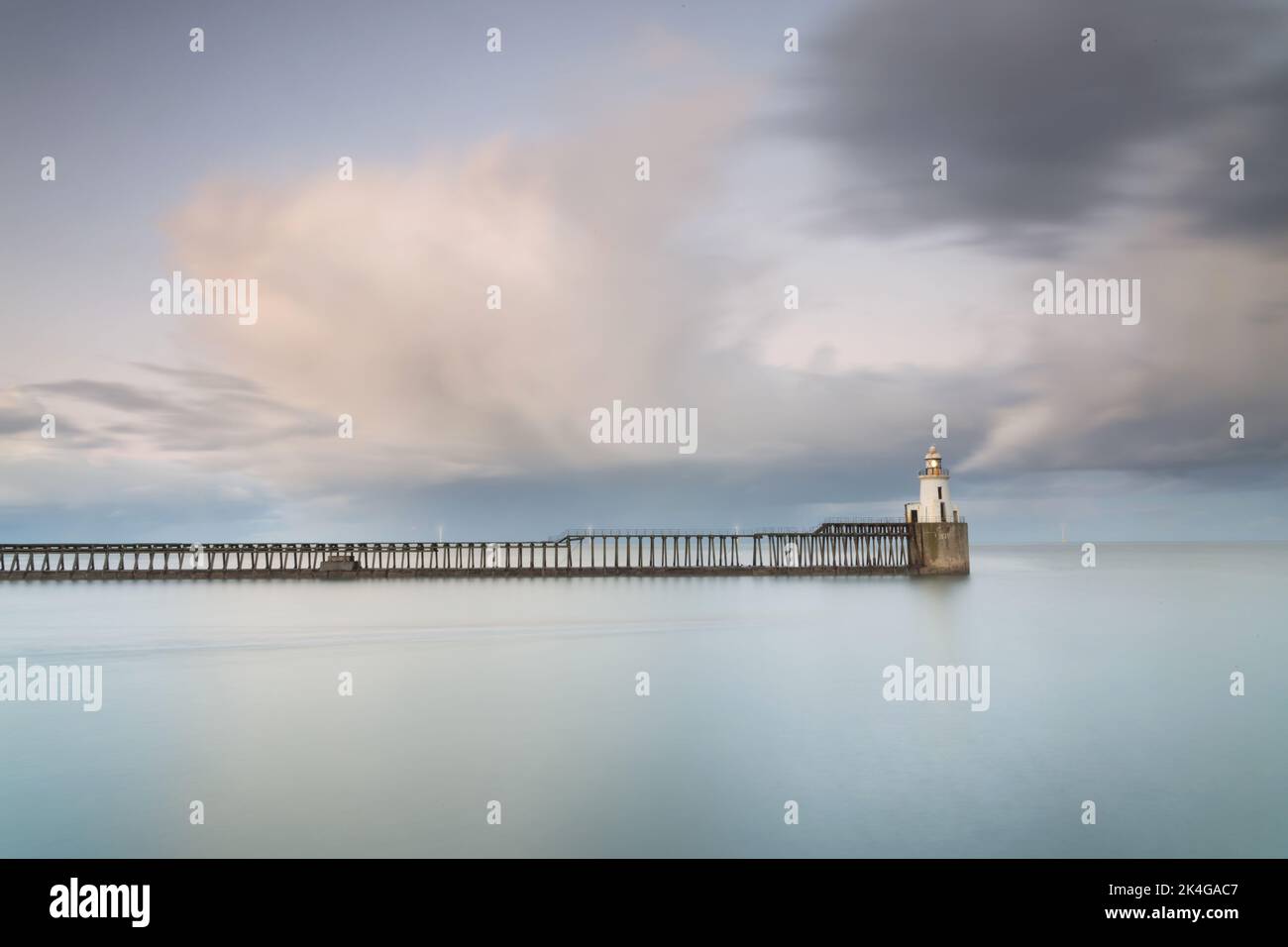 Une longue exposition au crépuscule par temps froid au port de Blyth, sur la côte de Northumberland, avec un quai en bois et un petit phare blanc Banque D'Images