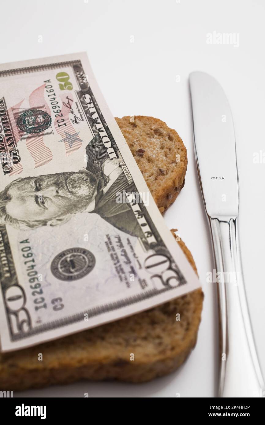 Billet de cinquante dollars US sur le dessus de la tranche de pain brun à côté du couteau en acier inoxydable. Banque D'Images
