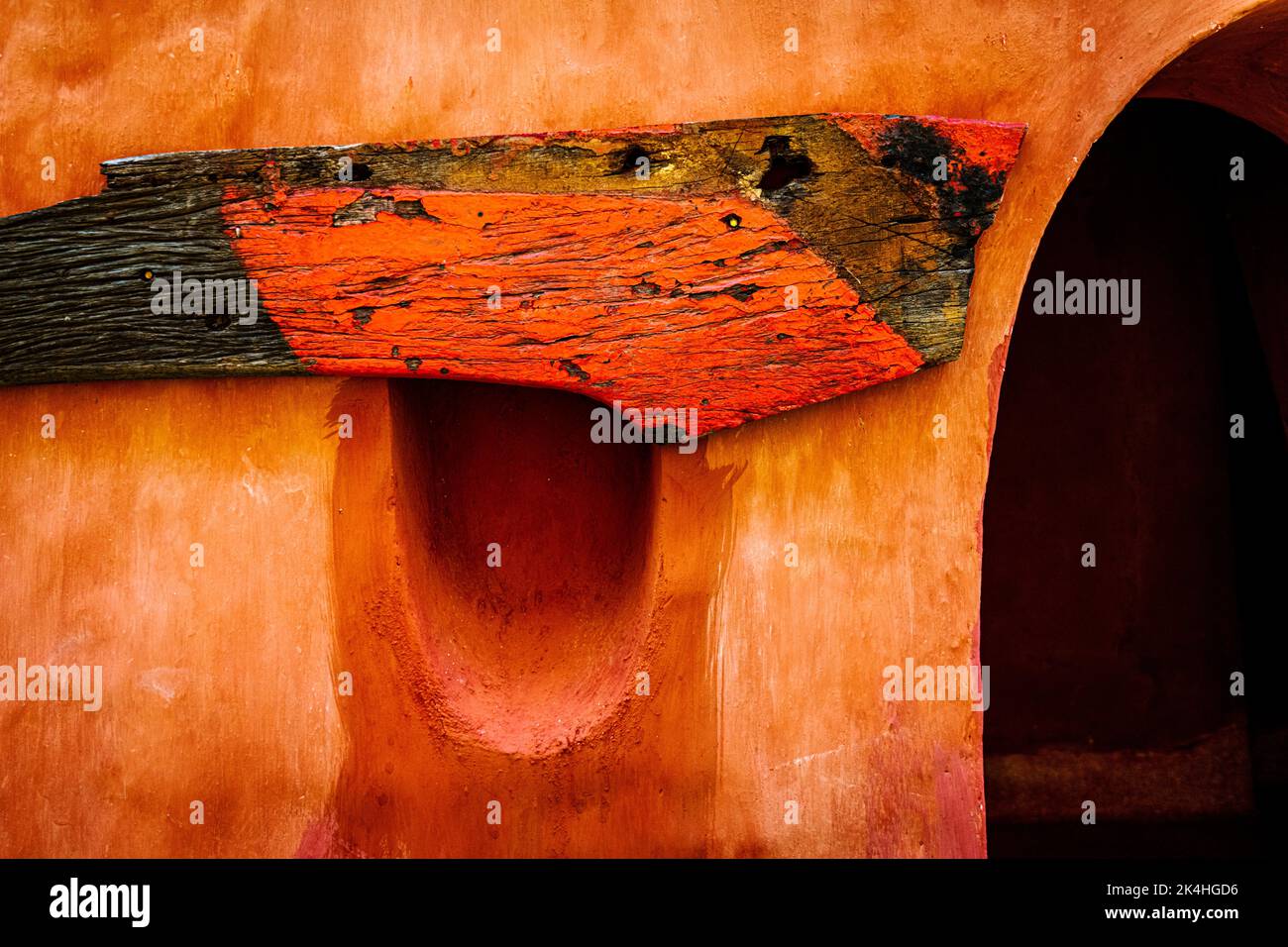 Un grand morceau de bois peint en orange et noir d'un vieux bateau de pêche est cloué au-dessus d'un trou comme un trou de peep à côté d'une entrée voûtée. Banque D'Images