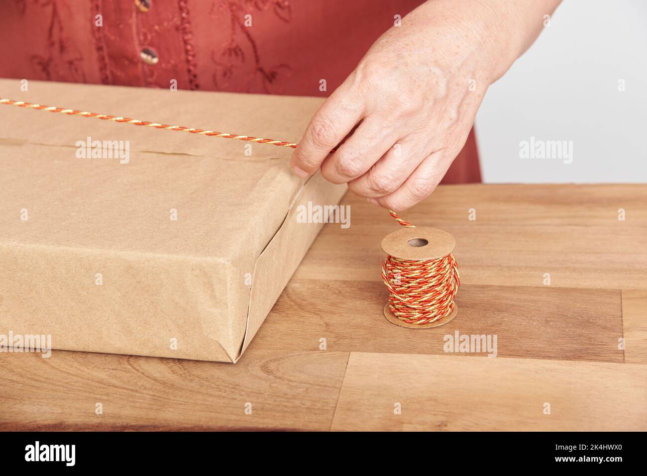 Femme adulte non reconnaissable qui enveloppe un cadeau de Noël, faisant un noeud avec un cordon décoratif. Design lumineux avec espace de copie. Banque D'Images