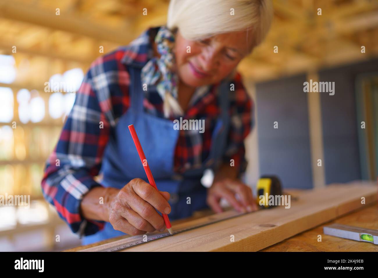 Femme senior mesurant le bois à l'intérieur de son éco-maison en bois écologique inachevé. Banque D'Images