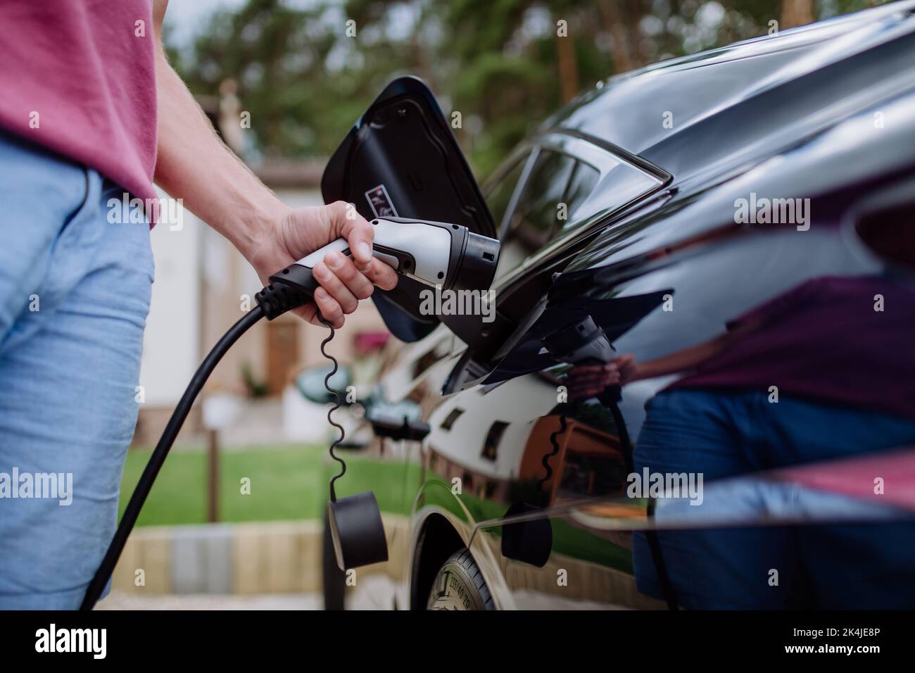 Homme tenant le câble d'alimentation électrique à la station de charge du véhicule électrique, à proximité Banque D'Images