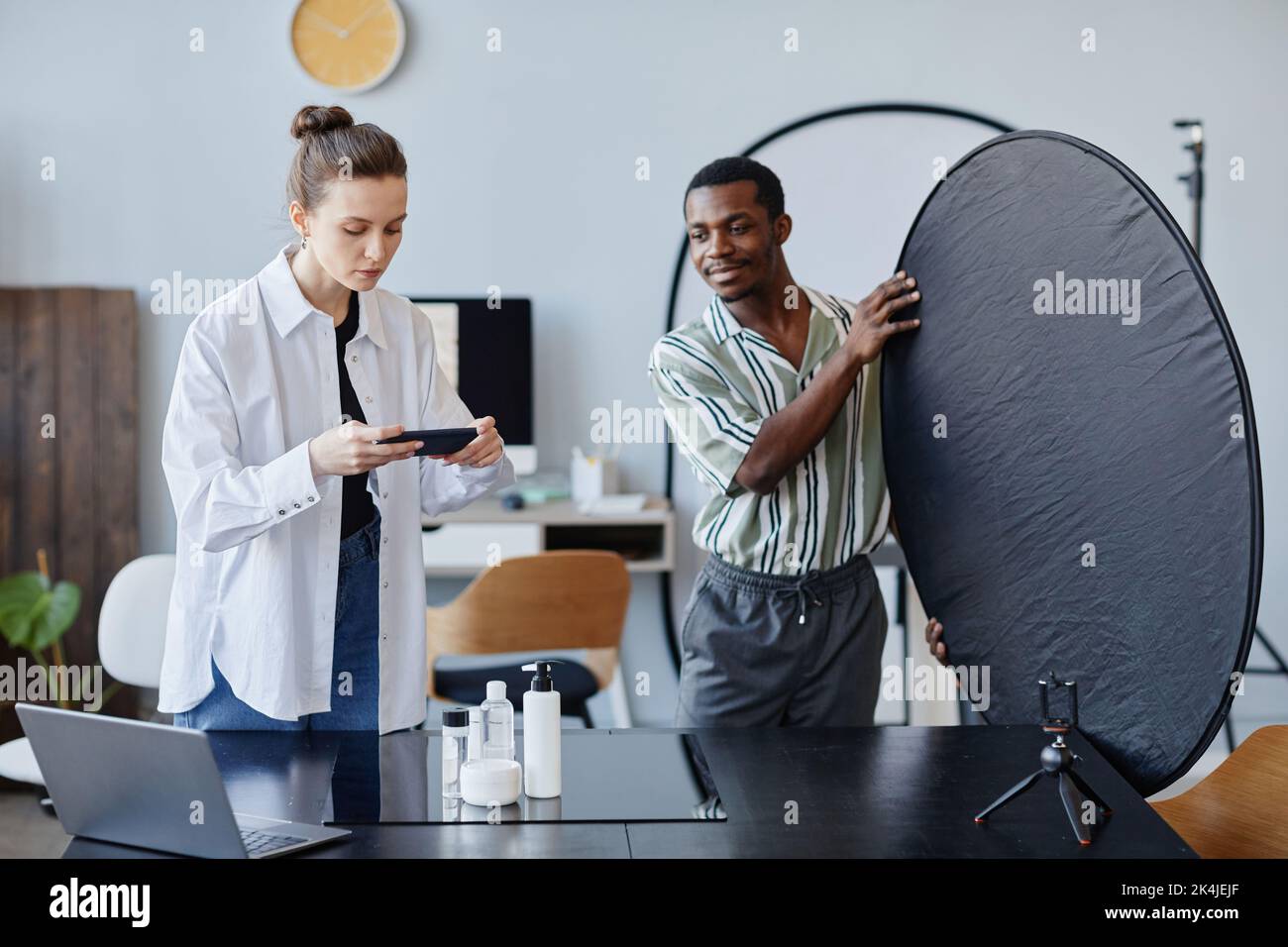 Portrait de deux jeunes photographes travaillant sur la photographie de produits en studio et utilisant un téléphone mobile pour la promotion des médias sociaux Banque D'Images
