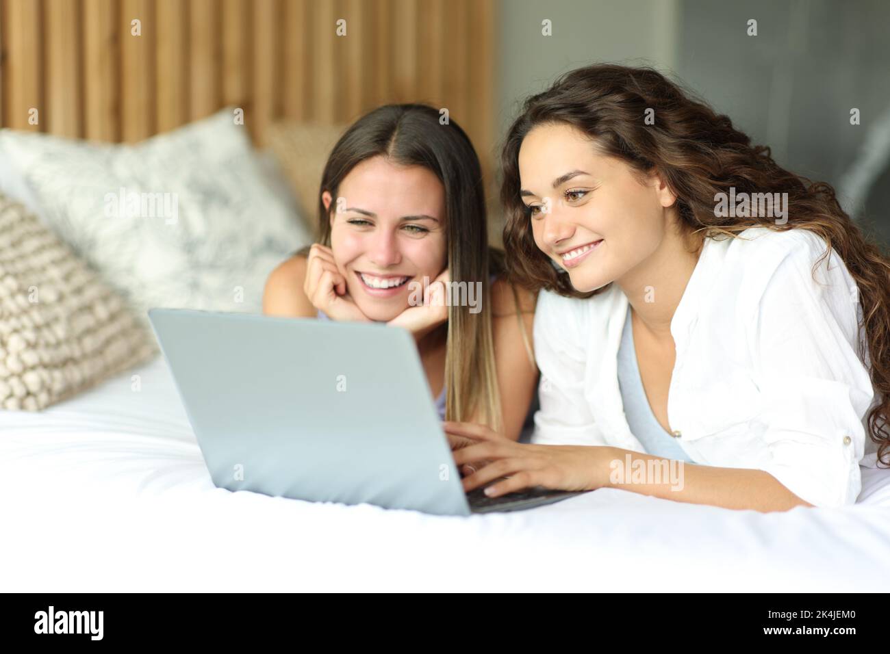 Deux femmes heureuses regardant les médias sur un ordinateur portable allongé sur un lit dans la chambre Banque D'Images