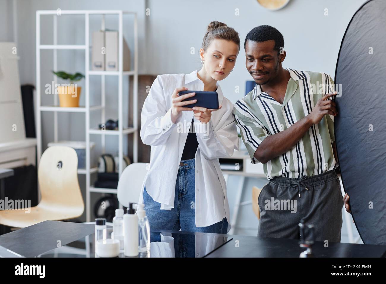 Portrait à la taille de deux jeunes travaillant sur la photographie de produit en studio et utilisant le téléphone mobile pour la promotion des médias sociaux, espace de copie Banque D'Images