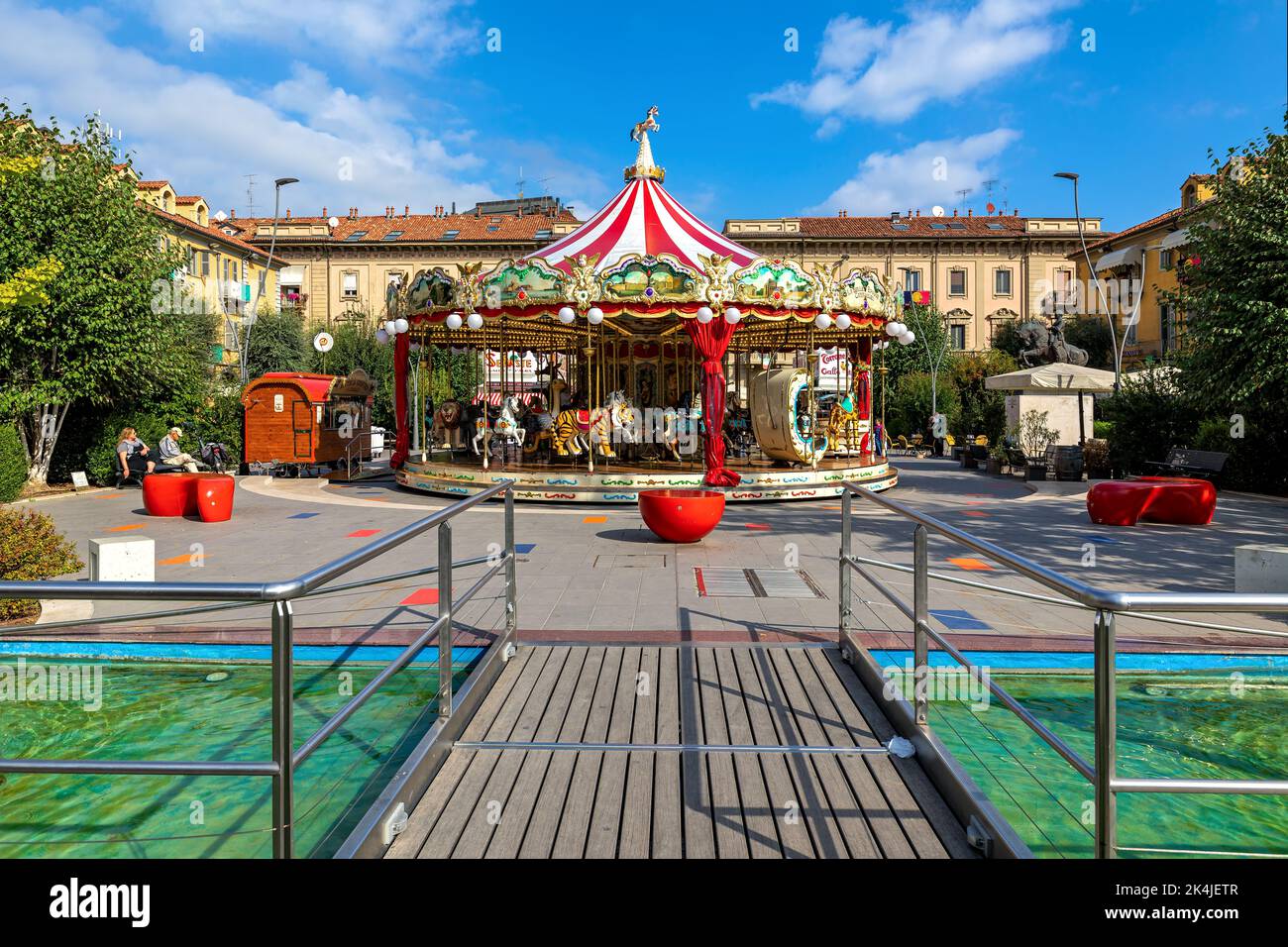 Carrousel coloré sur la petite piazza avec fontaine moderne à Alba - ville dans le Piémont, en Italie du Nord. Banque D'Images