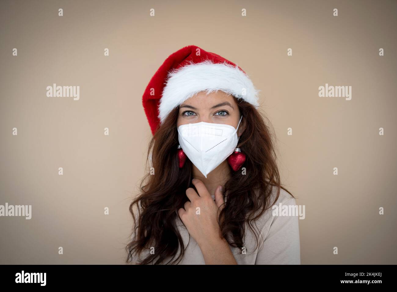 jolie jeune femme avec chapeau de noël porte un masque de visage, un masque de protection pour ne pas être infectée et est debout devant un fond marron Banque D'Images