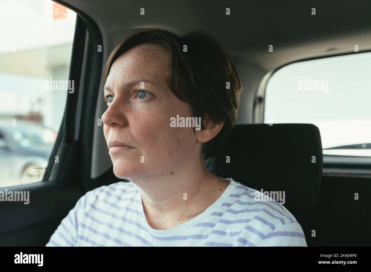 Femme assise à l'arrière de la voiture de tourisme et regardant par la fenêtre du véhicule, foyer sélectif Banque D'Images