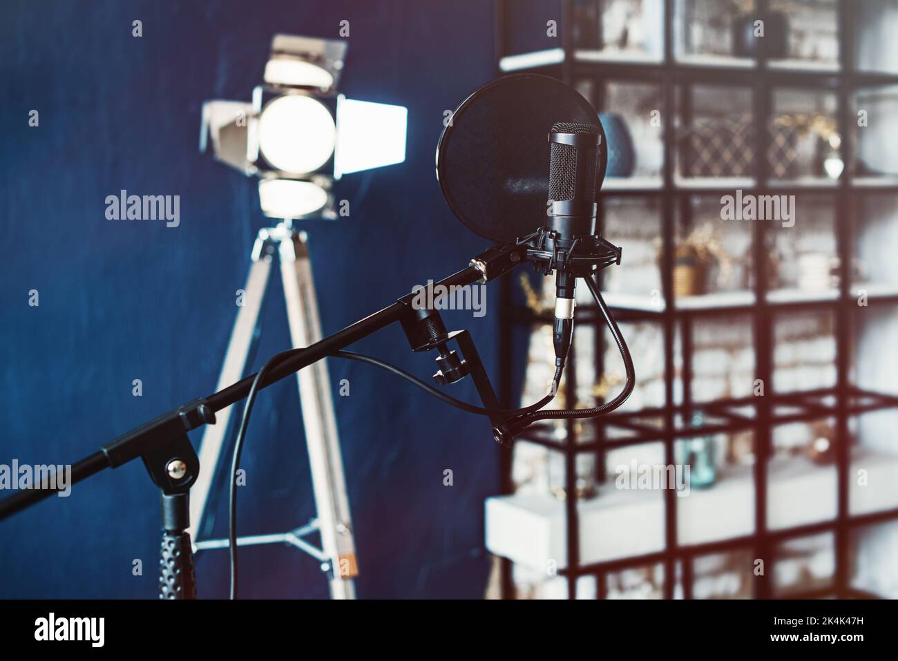 Microphone condensateur studio avec filtre pop et support anti-vibration pour l'enregistrement en direct. Mur bleu et lumière décorative sur fond Banque D'Images