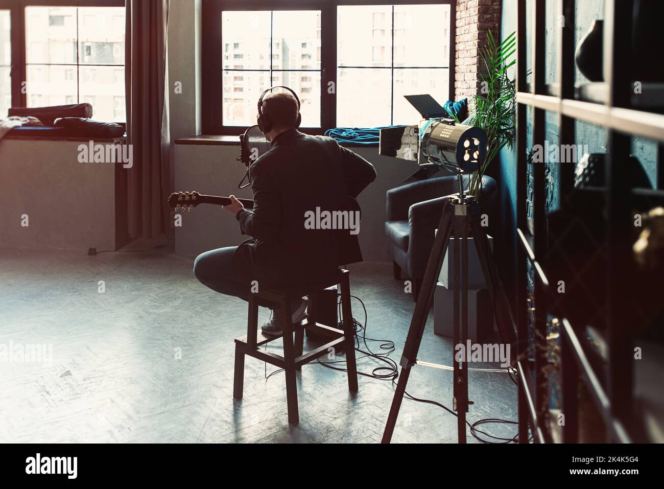 Homme chanteur assis sur un tabouret dans un casque avec une guitare enregistrant une piste dans un studio à domicile Banque D'Images