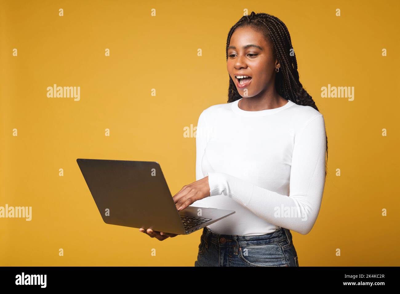 Une étudiante afro-américaine heureuse et excitée ne peut pas croire ses yeux, elle a ouvert la bouche, debout avec un ordinateur portable ouvert et en vérifiant les notes, se sentant heureuse de passer l'examen, concept de victoire Banque D'Images