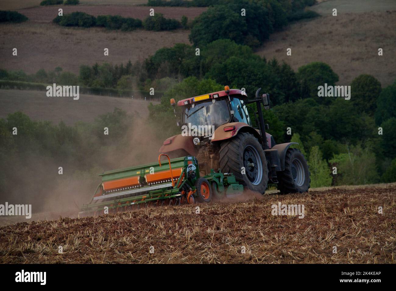 Tracteur hersant un sol brun rougeâtre, poussiéreux et argileux dans un paysage vallonné Banque D'Images