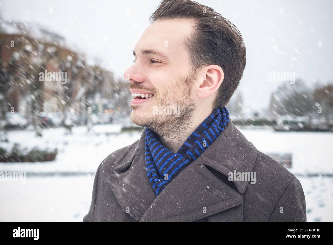 Portrait d'un jeune homme beau avec une barbe souriante en riant dans la neige d'hiver Banque D'Images