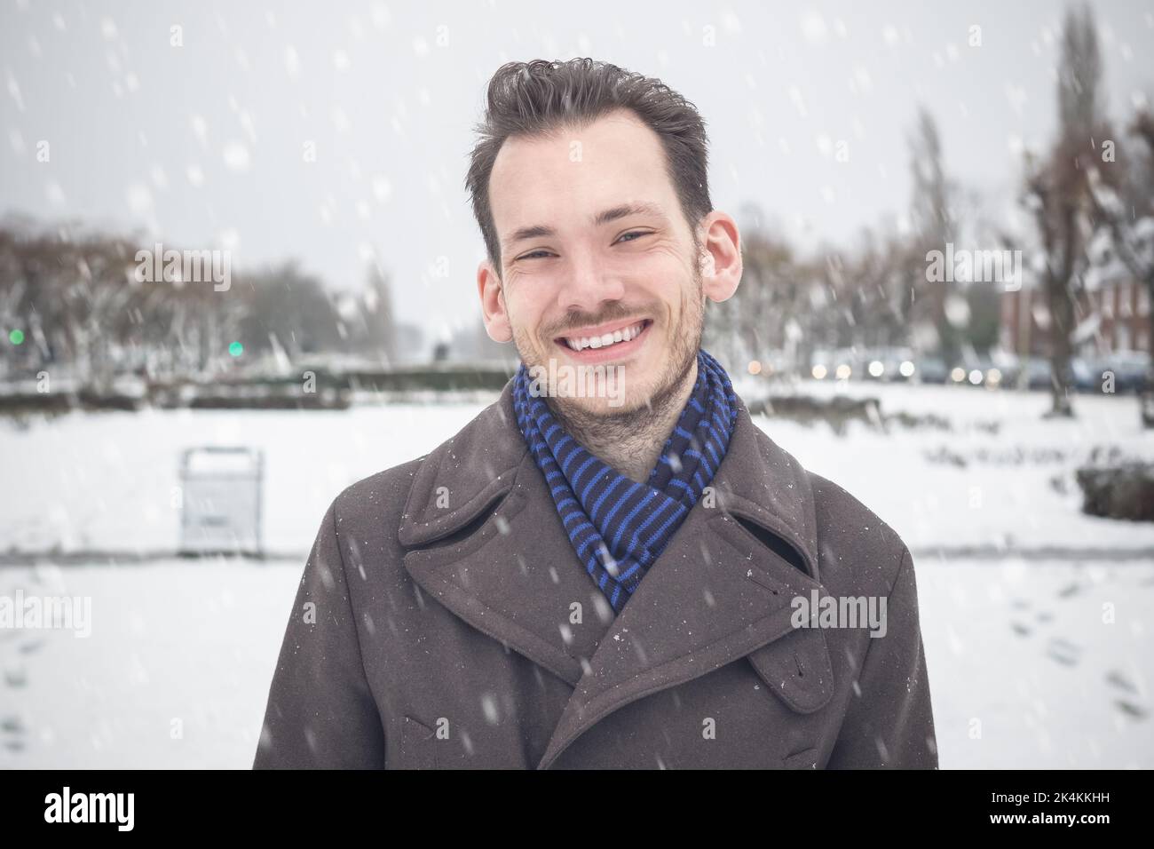 Portrait d'un jeune homme beau avec une barbe souriante en regardant l'appareil photo dans la neige d'hiver Banque D'Images