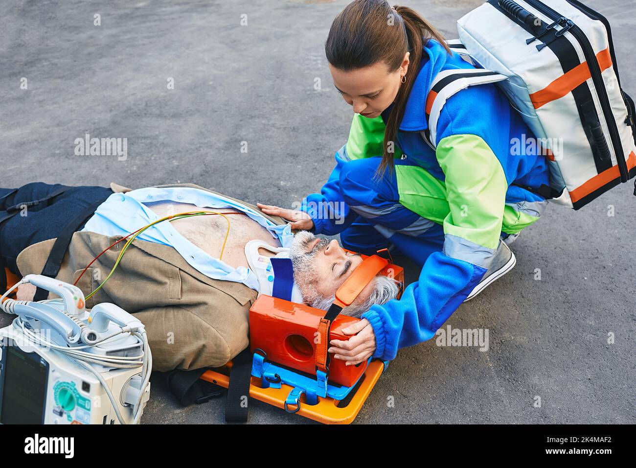 Femme paramédical fixant la tête de la victime mâle avec une blessure au cou couché sur le brancard d'ambulance. Premiers soins avec un collier cervical et un défibrillateur Banque D'Images