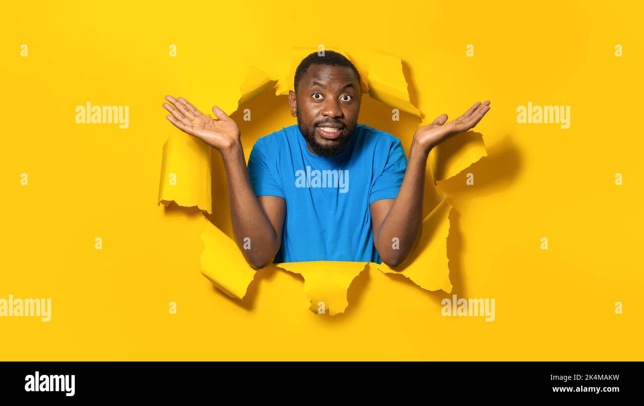 Un homme afro-américain se propageait les mains tout en se plaignant, posant dans un trou de papier jaune déchiré Banque D'Images