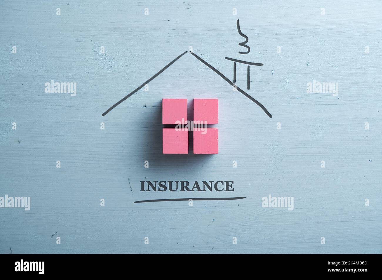 Maison faite de blocs de bois roses et un toit dessiné à la main coupé dans un fond en bois bleu pastel avec un panneau d'assurance sous la maison. Banque D'Images