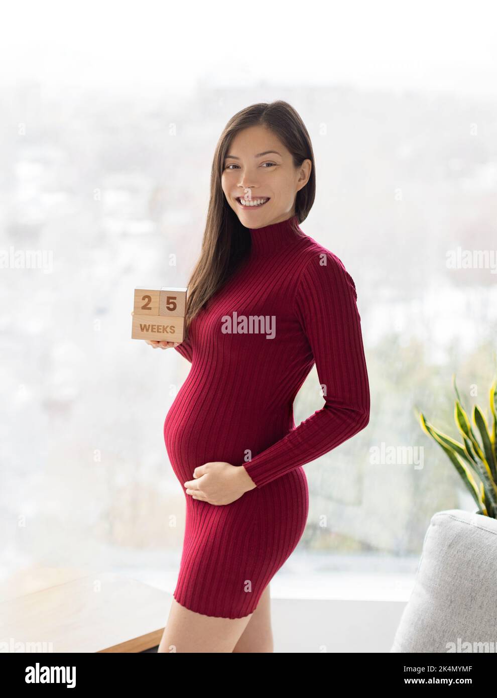 Femme enceinte asiatique montrant 25 semaines de grossesse bosse pour maternité photoshoot tenant des blocs de bois signe heureux. Recadrage vertical Banque D'Images
