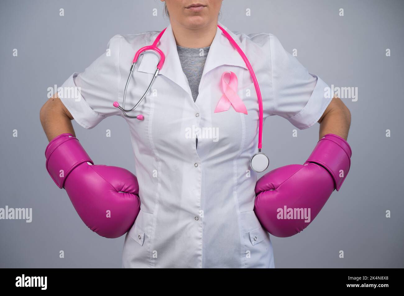 Femme médecin sans visage en gants de boxe rose avec un ruban rose sur fond gris. Lutte contre le cancer du sein. Banque D'Images Femme médecin sans visage en gants de boxe rose avec un ruban rose sur fond gris. Lutte contre le cancer du sein. Banque D'Images