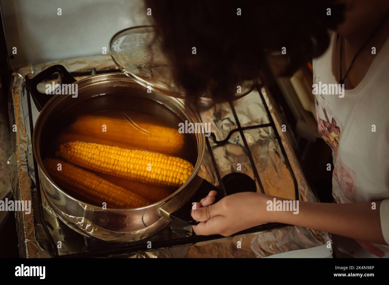 L'hôtesse regarde dans un pot avec du maïs cuit sur la cuisinière à la maison Banque D'Images